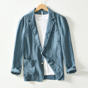 Giacca blazer casual blu in lino, con tasche frontali e maniche arrotolate, appesa su gruccia. Perfetta per look eleganti e informali.