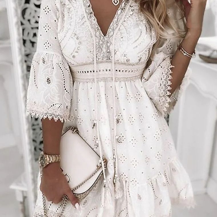 Abito bianco in pizzo con dettagli floreali, maniche a campana e scollo a V, abbinato a borsa a tracolla chiara. Elegante moda estiva femminile.