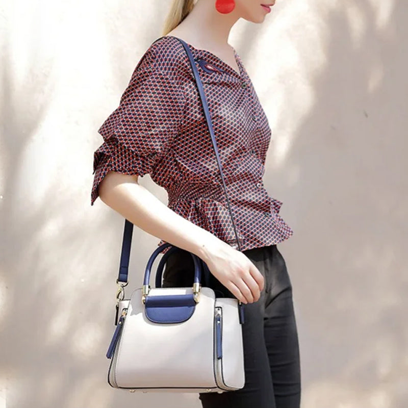 Donna con borsa a tracolla bianca e blu, camicia a fantasia rossa, pantaloni neri. Accessorio moda elegante, perfetto per look casual chic.