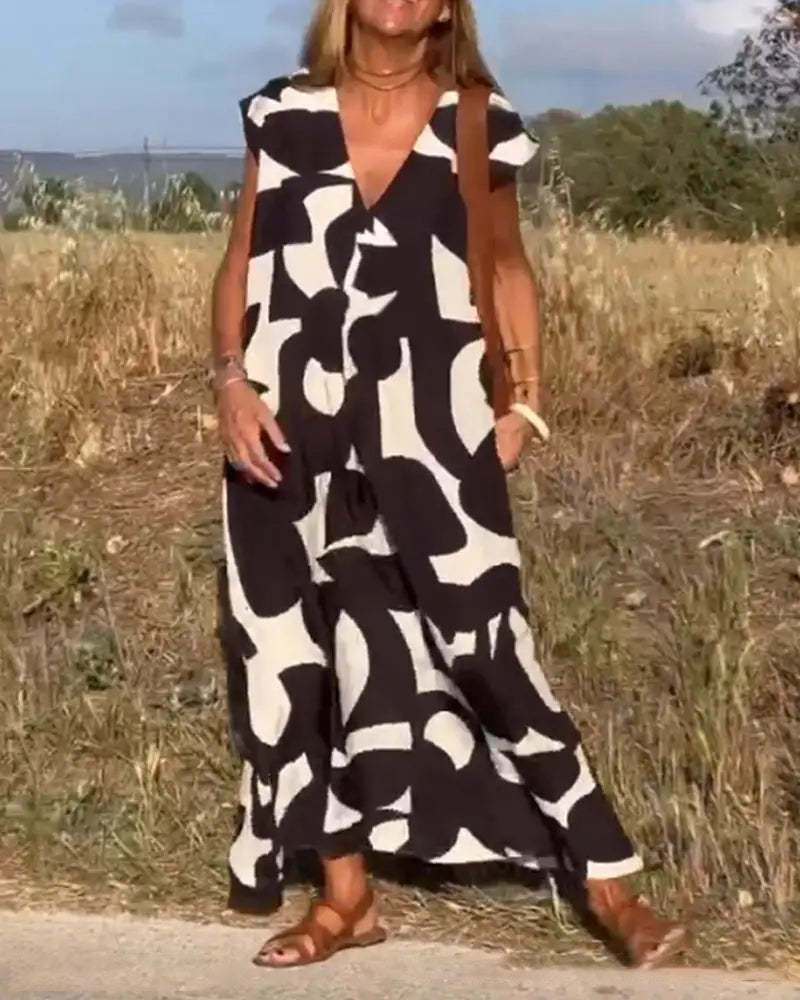 Donna con abito lungo bianco e nero a motivi astratti, sandali marroni, in un campo estivo. Moda estiva, abbigliamento casual elegante.