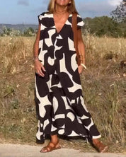 Donna con abito lungo bianco e nero a motivi astratti, sandali marroni, in un campo estivo. Moda estiva, abbigliamento casual elegante.