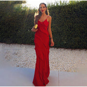 Donna in abito lungo rosso elegante con volant, borsa dorata, sfondo di siepe verde. Moda serale, abbigliamento da cerimonia, stile glamour.