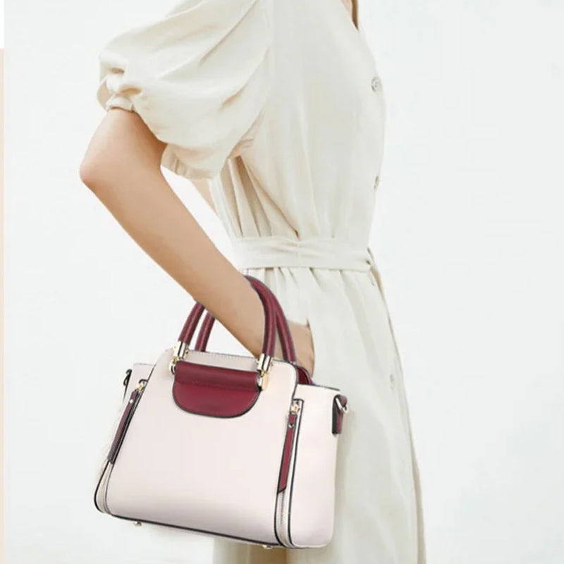 Donna con abito bianco avorio indossa borsa a mano elegante bicolore, manici marroni e dettagli dorati. Accessorio moda femminile chic.