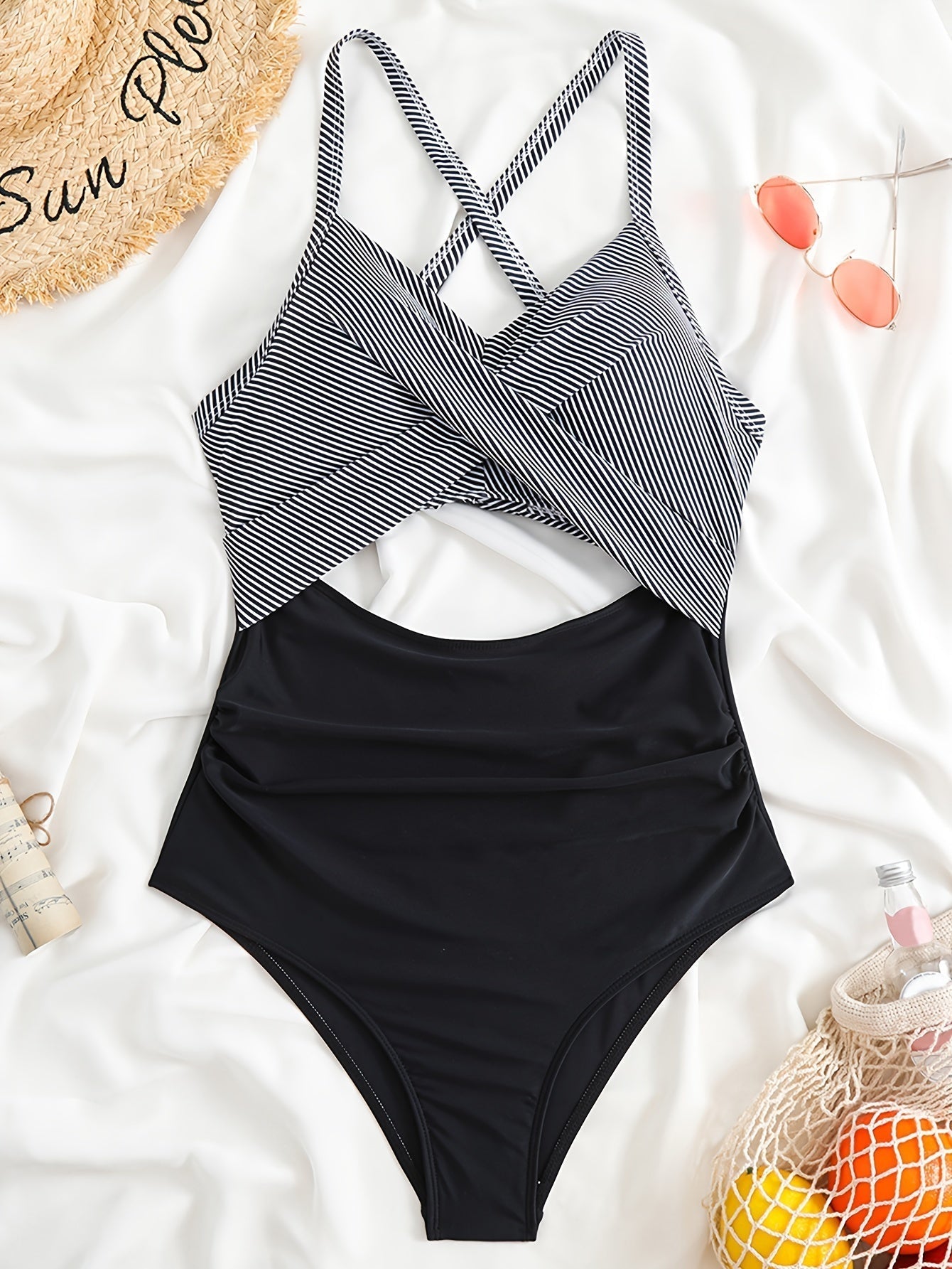 Costume intero donna a righe bianche e nere, design incrociato, su sfondo bianco con accessori estivi. Moda mare, abbigliamento da spiaggia.