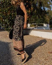 Donna con gonna lunga a motivi geometrici, top nero e espadrillas nere su ghiaia. Moda estiva, abbigliamento casual chic, stile boho.