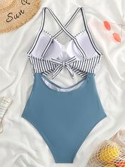 Costume intero donna a righe bianche e nere con fiocco, parte inferiore blu, su sfondo bianco con occhiali da sole e cappello di paglia.