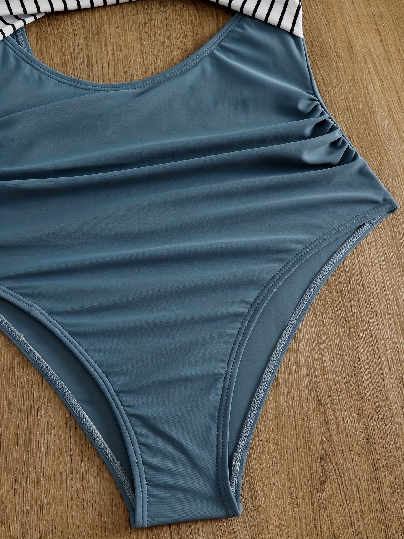 Costume intero blu con dettagli a righe bianche e nere, tessuto liscio, design elegante, perfetto per la spiaggia o la piscina.