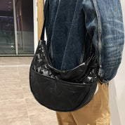 Borsa a tracolla nera in nylon lucido, indossata su giacca di jeans e pantaloni beige. Design moderno, ideale per moda urbana e casual.