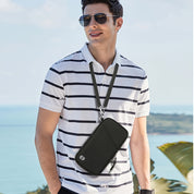 Uomo con polo a righe bianche e nere, indossa occhiali da sole e borsa a tracolla nera. Sfondo di mare e vegetazione tropicale.