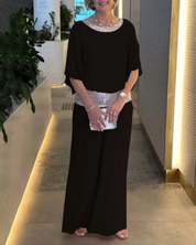 Abito elegante nero da donna con dettagli scintillanti, clutch argentata, indossato in un ambiente moderno con piante decorative.