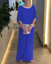 Donna in abito blu elegante con dettagli scintillanti, in piedi in un corridoio moderno. Accessori: pochette e orologio. Look da sera sofisticato.