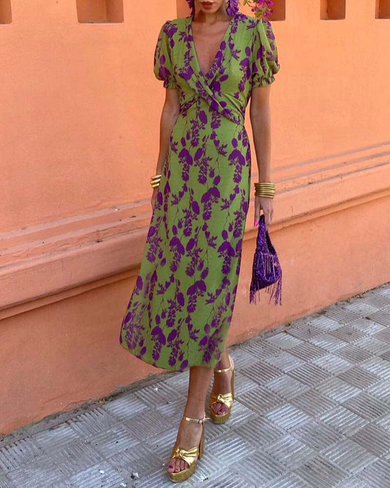 Abito lungo verde con stampa floreale viola, maniche a sbuffo, borsa frange viola, sandali dorati. Moda estiva donna, look elegante e colorato.
