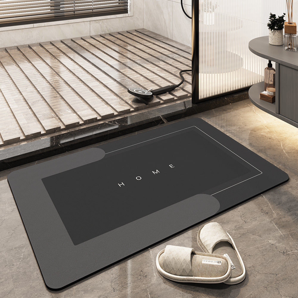 Tappetino da bagno nero con scritta "HOME", design moderno, antiscivolo, posizionato su pavimento in marmo, accanto a pantofole beige.