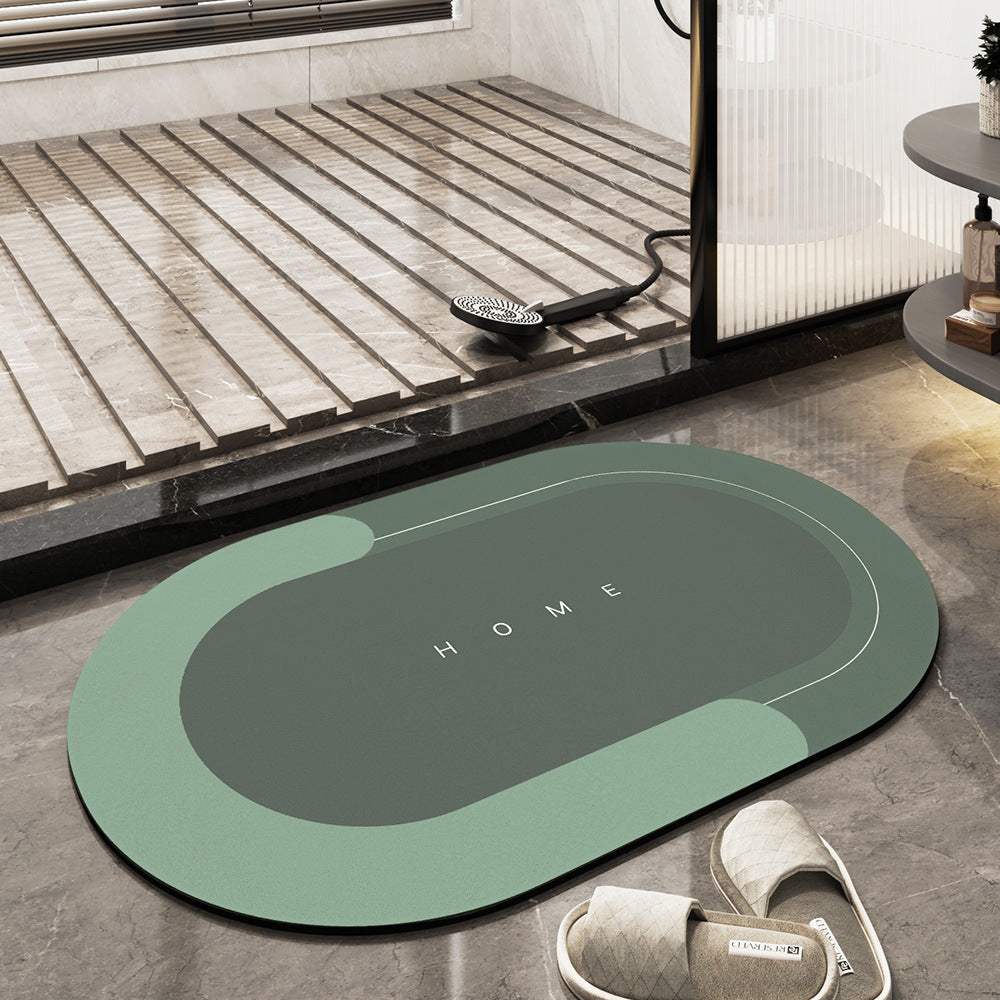Tappeto da bagno ovale verde con scritta "HOME", posizionato su pavimento in marmo grigio, accanto a doccia moderna e pantofole beige.