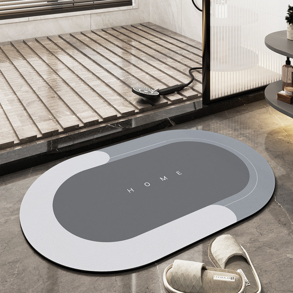 Tappeto da bagno ovale grigio con scritta "HOME", design moderno, antiscivolo, posizionato su pavimento in marmo vicino a doccia e pantofole.