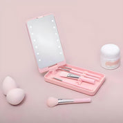 Set trucco rosa con specchio illuminato, pennelli, spugne e crema viso su sfondo rosa. Kit cosmetico portatile per make-up professionale.