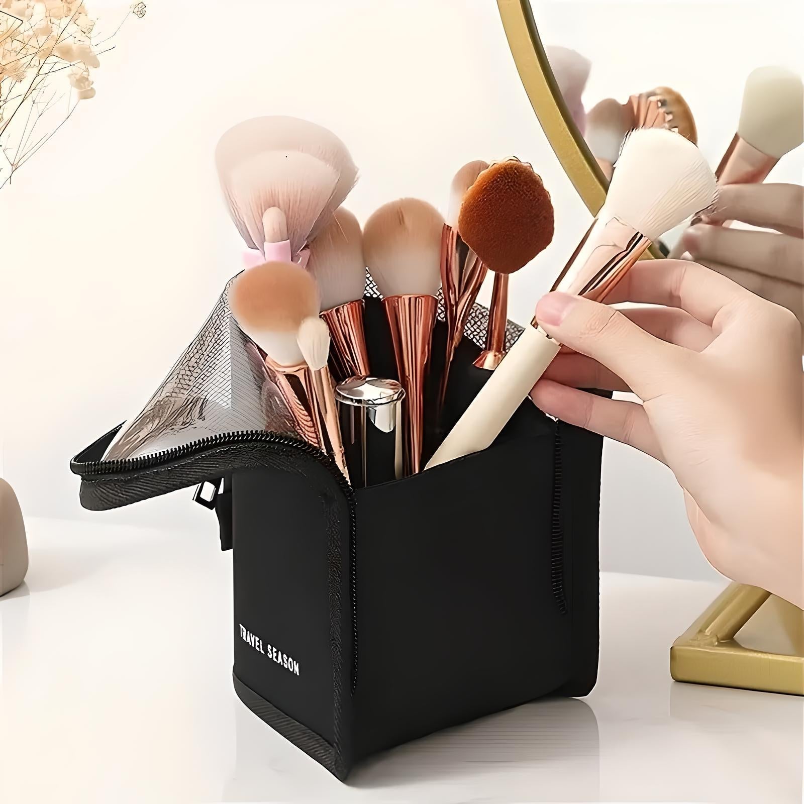 Set di pennelli da trucco in borsa nera con cerniera, specchio dorato riflettente, mano che prende un pennello. Accessori cosmetici eleganti e pratici.