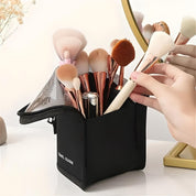 Set di pennelli da trucco in borsa nera con cerniera, specchio dorato riflettente, mano che prende un pennello. Accessori cosmetici eleganti e pratici.