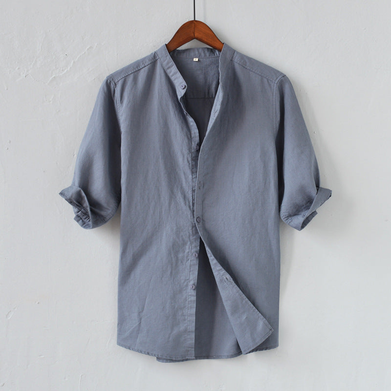Camicia uomo grigia in cotone, maniche lunghe arrotolate, colletto alla coreana, design casual elegante, appesa su gruccia di legno.
