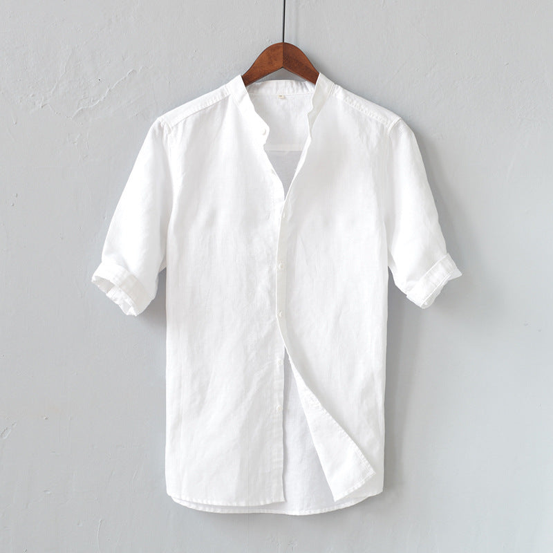 Camicia bianca in lino da uomo, maniche corte, colletto alla coreana, appesa su gruccia di legno, sfondo grigio. Elegante e casual.