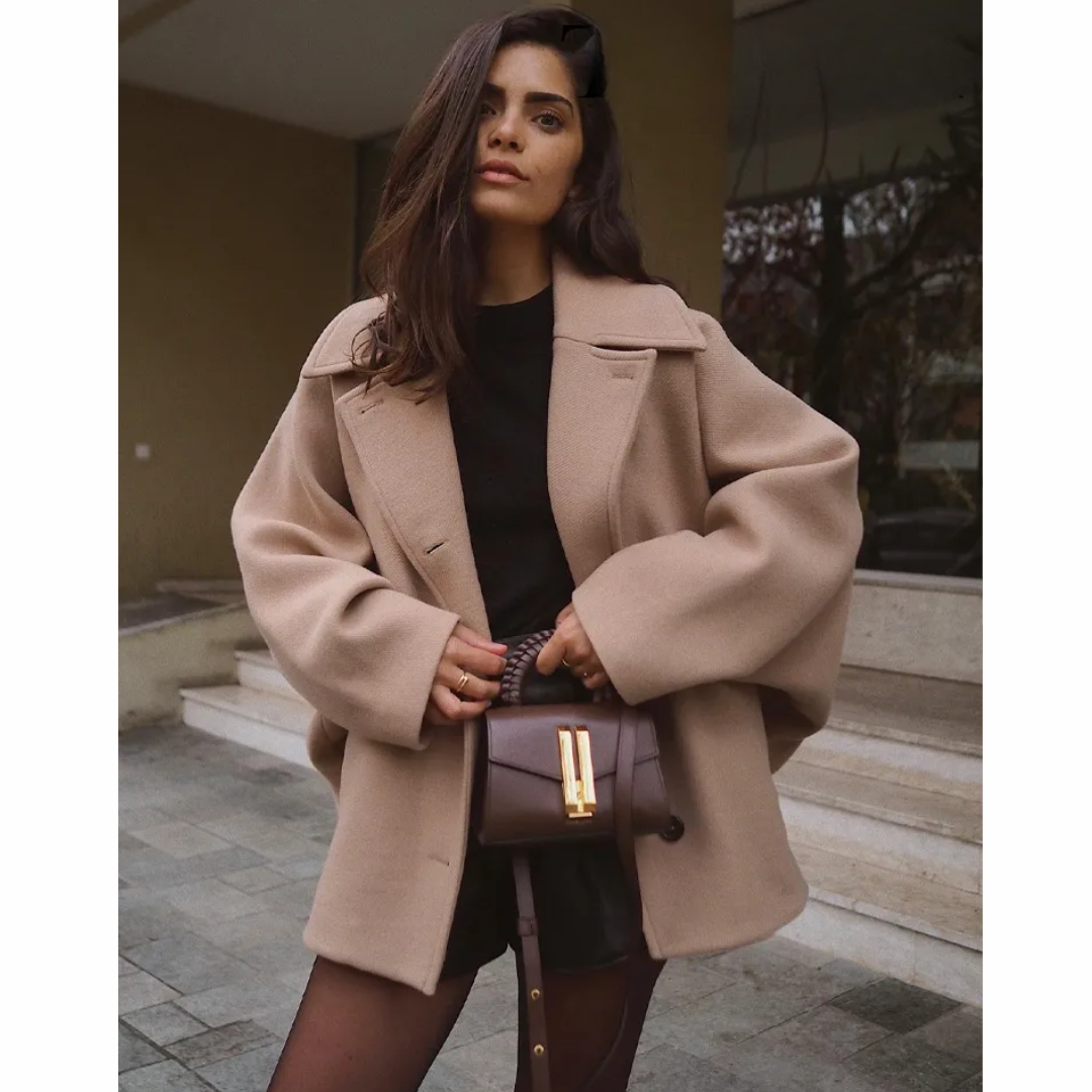Donna con cappotto beige oversize, borsa a tracolla marrone e abito nero. Moda autunnale elegante, look urbano chic. Outfit casual sofisticato.