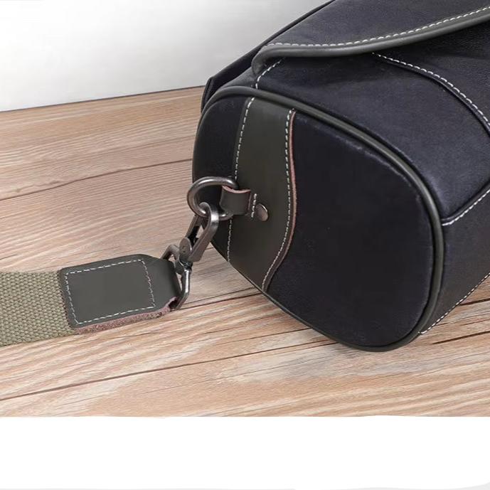 Borsa a tracolla in pelle nera su tavolo di legno, con cuciture bianche e tracolla regolabile. Design elegante e moderno per uomo e donna.