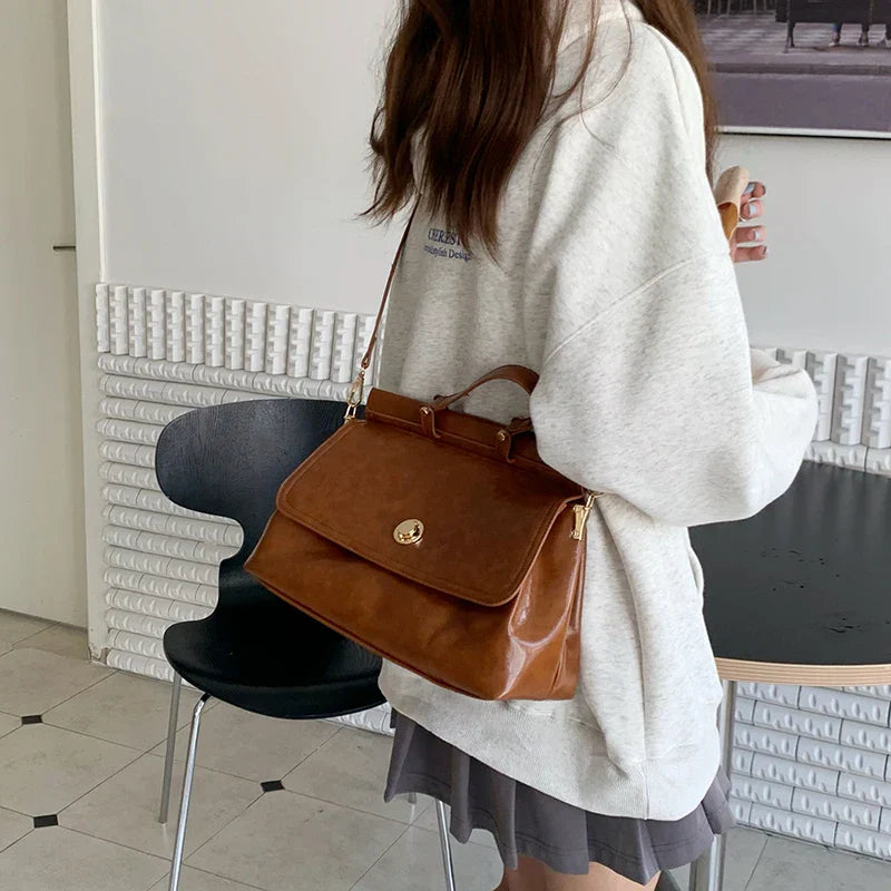 Donna con borsa a tracolla in pelle marrone, indossa felpa grigia e gonna corta. Moda casual femminile, accessori eleganti, stile urbano.
