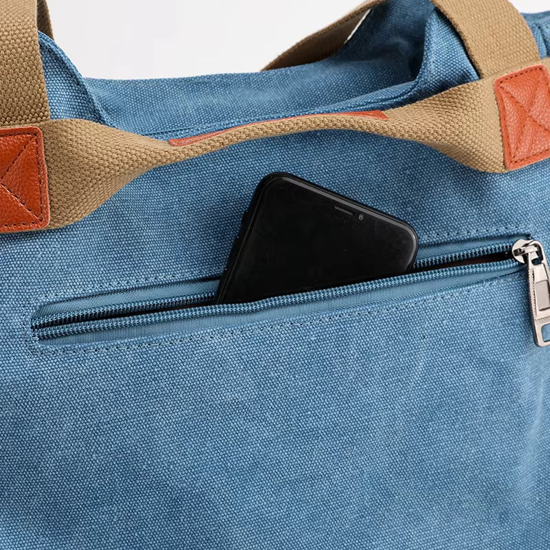 Borsa in tela blu con manici marroni, tasca con cerniera contenente uno smartphone nero. Design elegante e pratico per uso quotidiano.