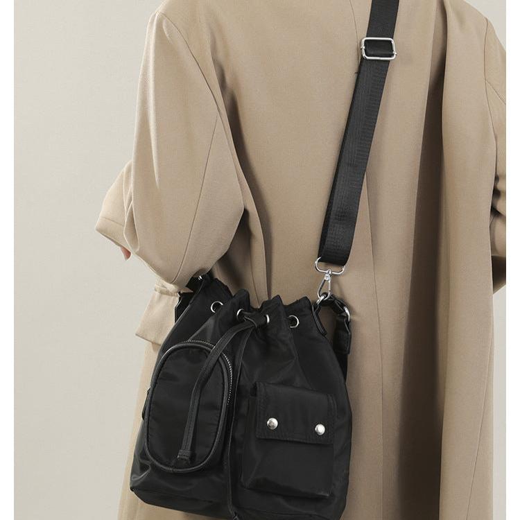 Cappotto beige con borsa a tracolla nera in nylon, design a secchiello, tasche frontali con bottoni, moda autunno inverno, accessori donna eleganti.
