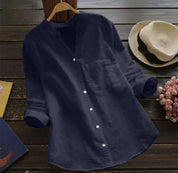 Camicia casual da donna blu scuro in cotone, maniche lunghe, colletto alla coreana, bottoni bianchi, su sfondo di legno con cappello e fiori.
