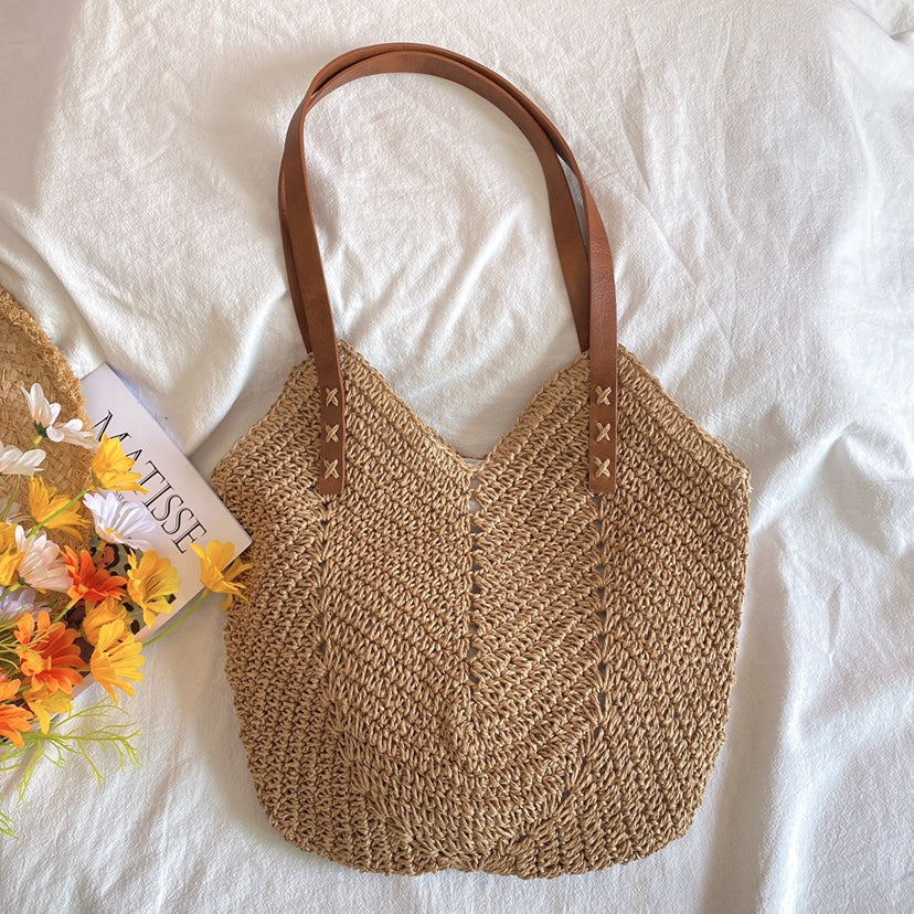 Borsa in paglia intrecciata con manici in pelle marrone, decorata con fiori gialli e libro. Perfetta per l'estate e lo shopping.