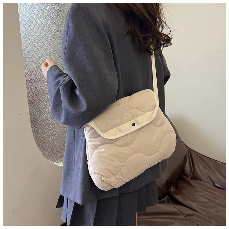 Donna con borsa a tracolla trapuntata beige, abbigliamento elegante grigio, sfondo interno. Accessorio moda femminile, stile casual chic.