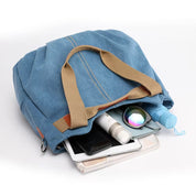 Borsa a tracolla in tela blu con manici beige, contenente smartphone, cosmetici, occhiali da sole e accessori. Ideale per viaggi e uso quotidiano.