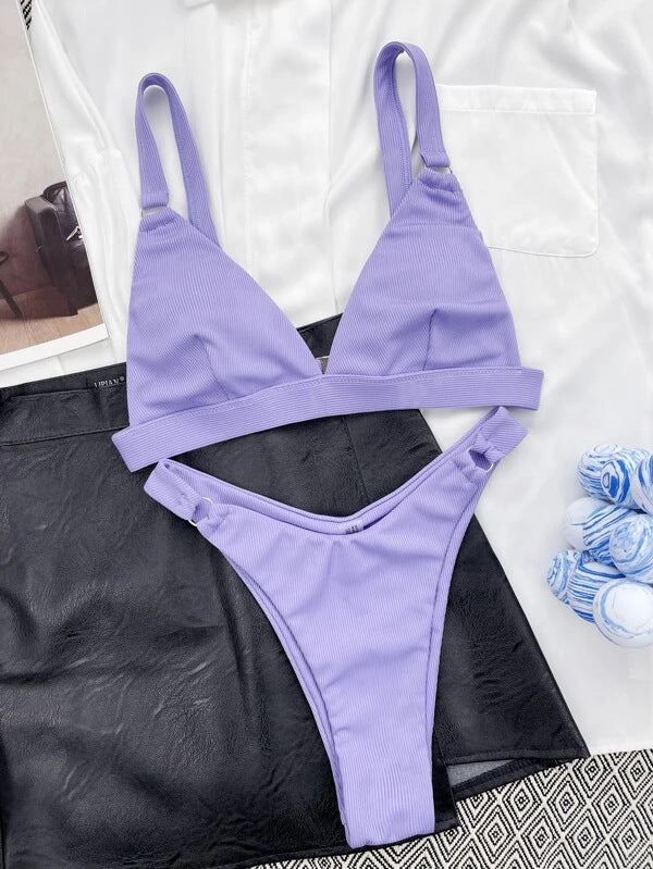 Bikini viola a due pezzi su sfondo bianco e nero, con reggiseno triangolare e slip a vita bassa. Tessuto a costine, stile estivo, moda mare.