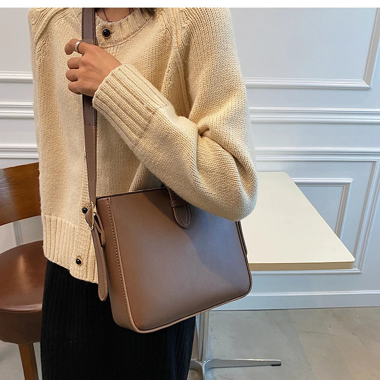 Borsa a tracolla marrone in pelle, indossata da una donna con maglione beige. Design elegante, perfetta per moda autunnale e look casual chic.