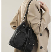 Donna con cappotto beige indossa zaino nero elegante in nylon, tasca frontale con zip, stile casual chic, moda autunno inverno.