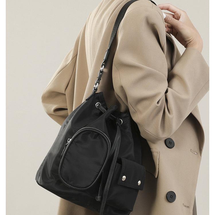 Donna con cappotto beige indossa zaino nero elegante in nylon, tasca frontale con zip, stile casual chic, moda autunno inverno.