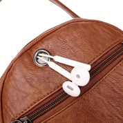 Zaino in pelle marrone con auricolari bianchi inseriti in un foro per cavi. Design elegante, ideale per viaggi e uso quotidiano. Accessorio moda pratico.