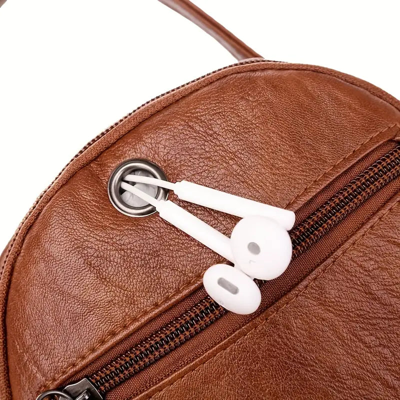 Zaino in pelle marrone con auricolari bianchi inseriti in un foro per cavi. Design elegante, ideale per viaggi e uso quotidiano. Accessorio moda pratico.