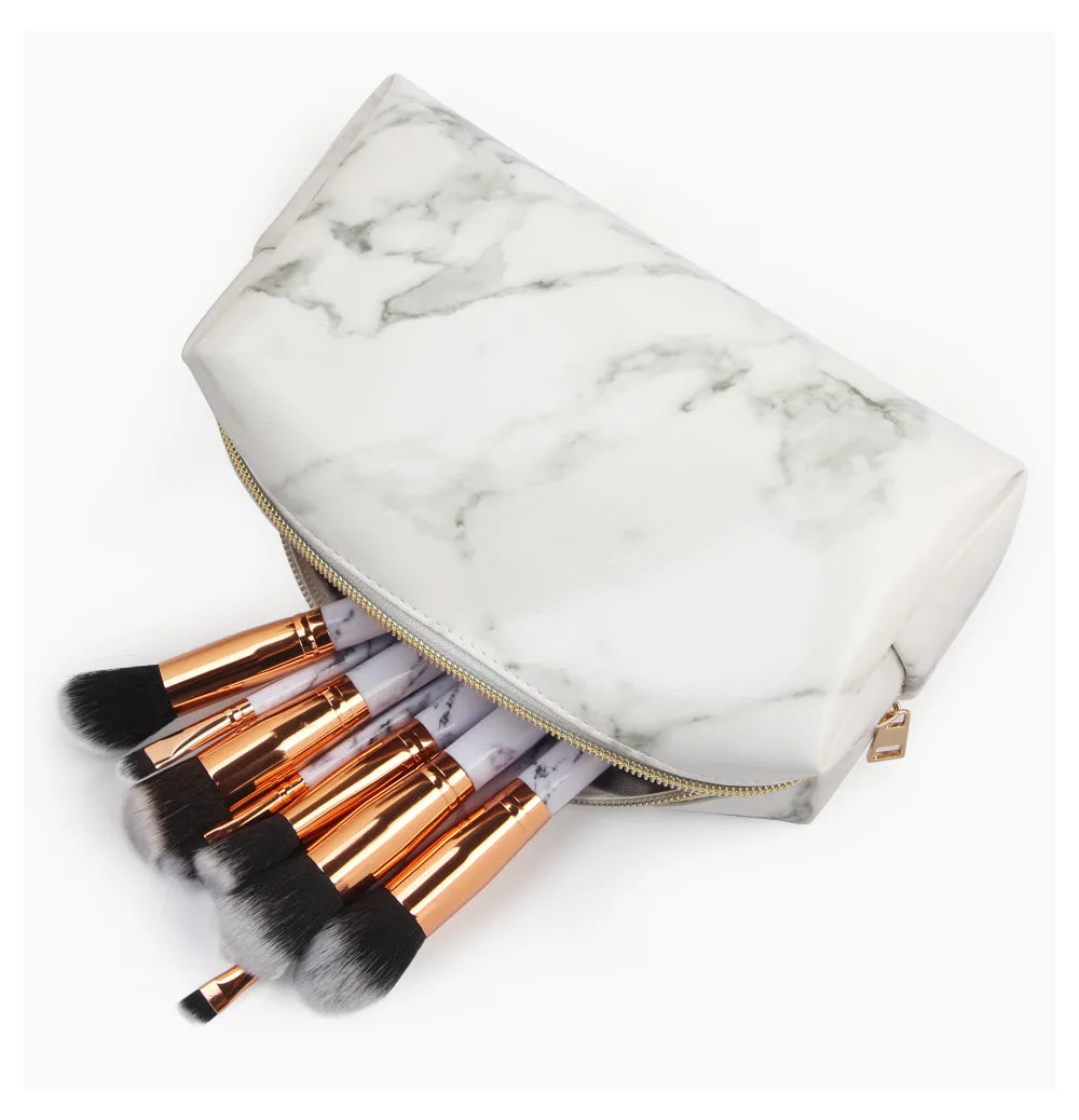 Set di pennelli trucco con manici dorati in pochette effetto marmo bianco. Accessori cosmetici eleganti per make-up professionale.