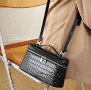 Borsa a tracolla in pelle nera con motivo coccodrillo, chiusura a zip e lucchetto, appoggiata su sedia. Accessorio moda elegante e versatile.