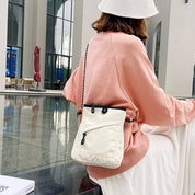 Donna con borsa a tracolla bianca, indossa felpa rosa e cappello bianco, seduta in ambiente moderno. Accessorio moda casual, stile urbano.