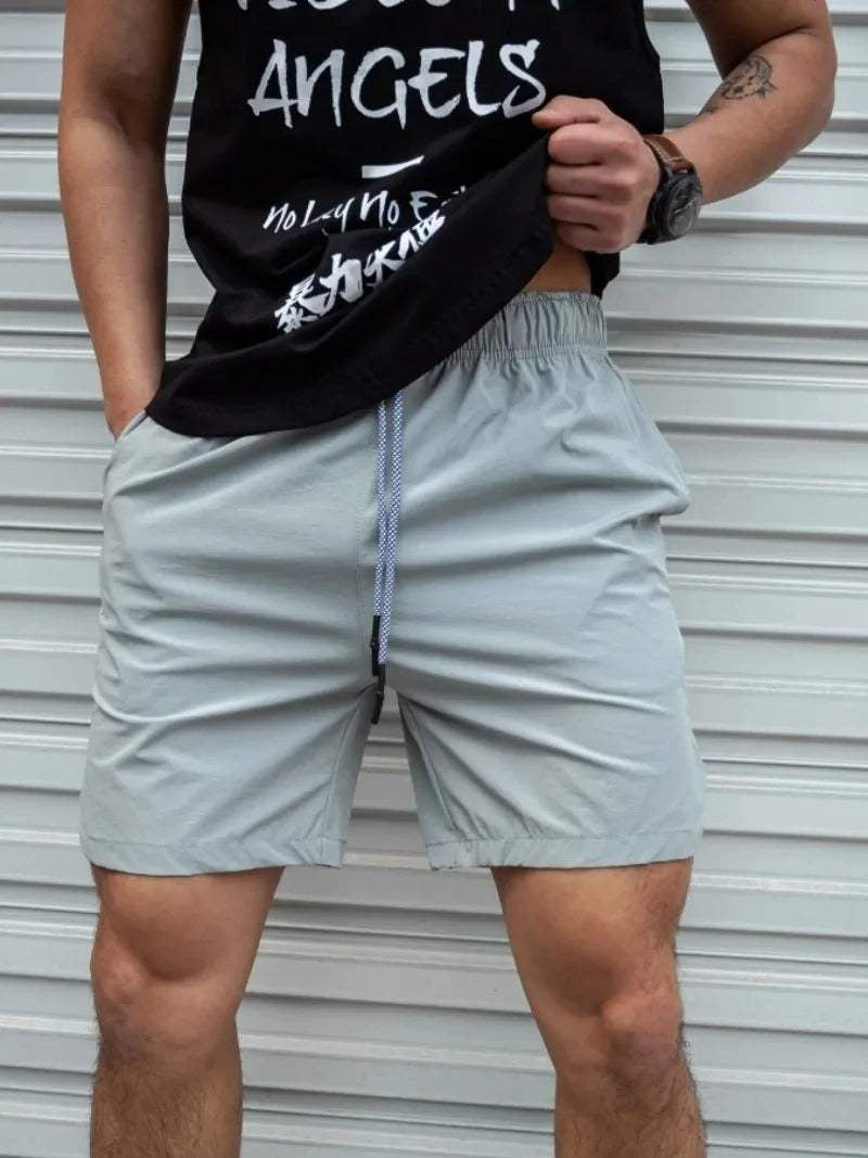Uomo in pantaloncini sportivi grigi e maglietta nera davanti a una porta bianca. Abbigliamento casual estivo, moda maschile.