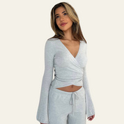 Donna con maglia grigia a maniche lunghe e pantaloni coordinati, posa su sfondo chiaro. Moda casual, abbigliamento comodo, stile elegante.