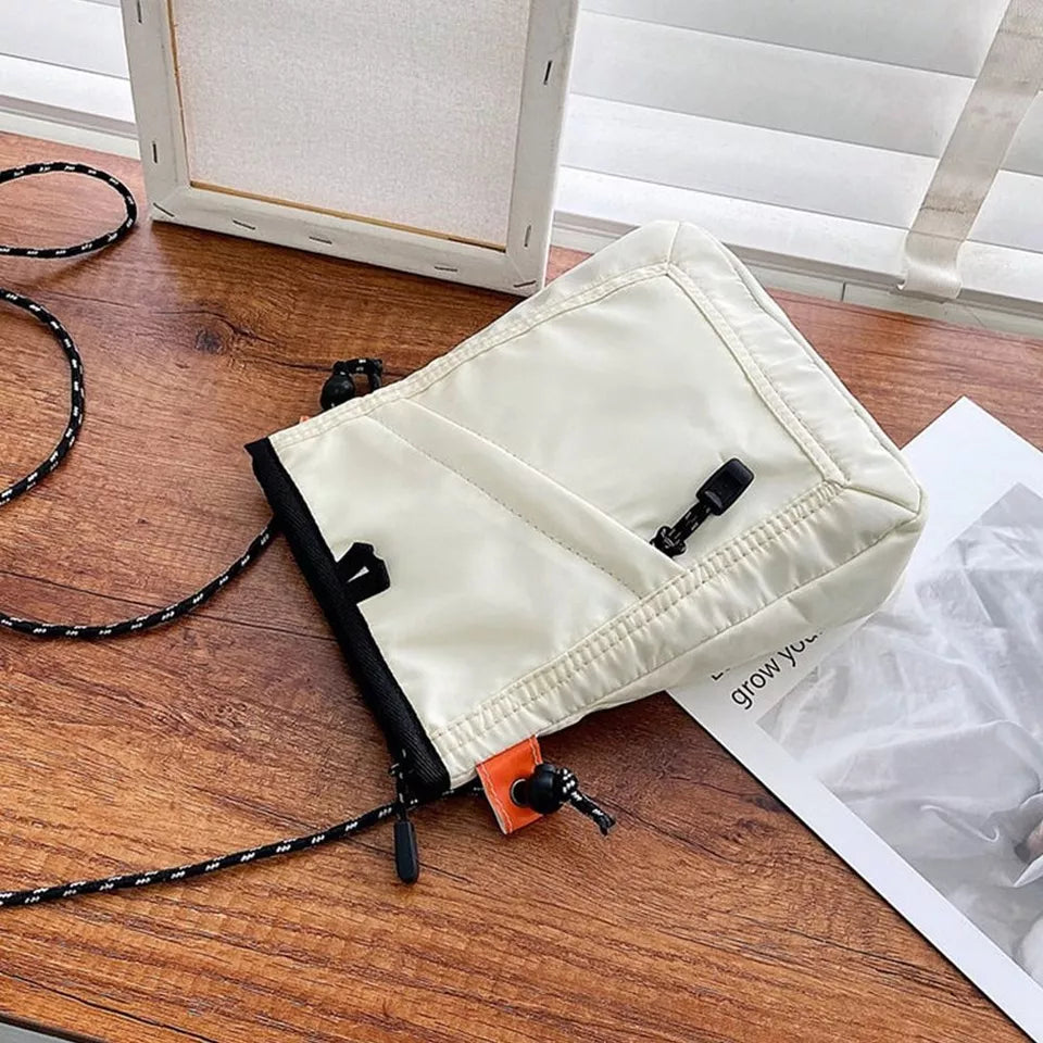 Borsa a tracolla bianca in nylon su tavolo di legno, con cerniera nera e cordino regolabile. Design moderno, ideale per moda urbana e viaggi.