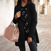 Donna con cappotto nero elegante, maglione con scritta "Paris", jeans scuri e borsa a mano beige. Moda autunnale, stile urbano chic.