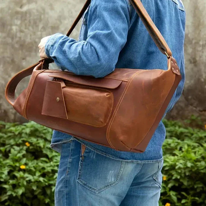 Uomo con borsa a tracolla in pelle marrone, tasca frontale con bottone, indossa giacca e jeans. Accessorio moda, stile casual, outdoor.