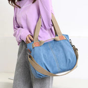Borsa a tracolla in denim blu con manici beige, indossata da una persona con maglia viola. Design casual, ideale per moda quotidiana.
