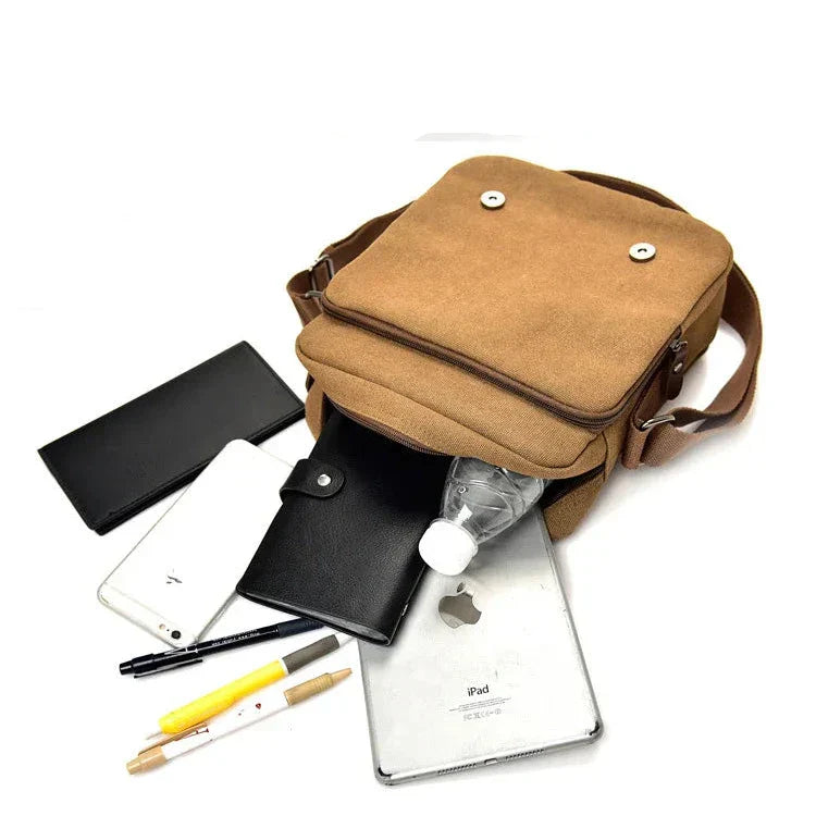 Borsa a tracolla marrone in tela con tasche multiple, contenente bottiglia d'acqua, iPad, smartphone, portafoglio nero e penne. Accessori moda uomo.