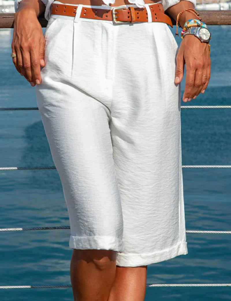 Pantaloncini bermuda bianchi da donna, eleganti e casual, con cintura marrone, perfetti per l'estate. Sfondo marino. Moda estiva femminile.